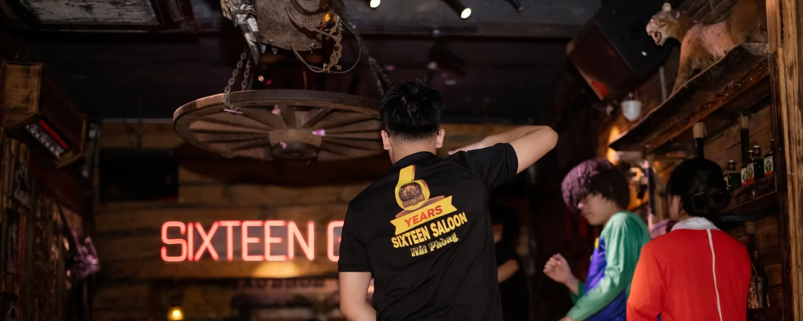 Biển chữ đỏ và bánh xe ngựa treo trần trong saloon Sixsense