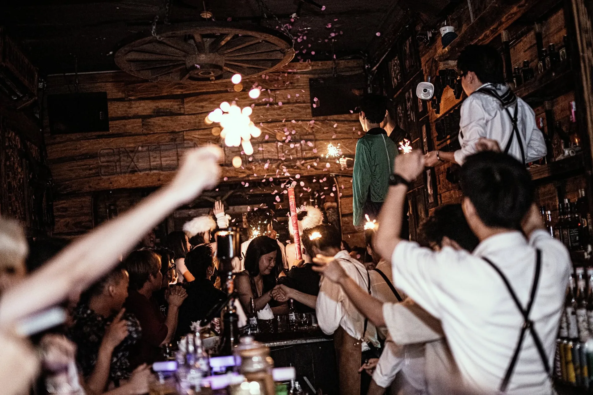 Đèn chùm bánh xe ngựa trên vách ván gỗ và đám đông giơ pháo que tại Sixsense Saloon Hải Phòng
