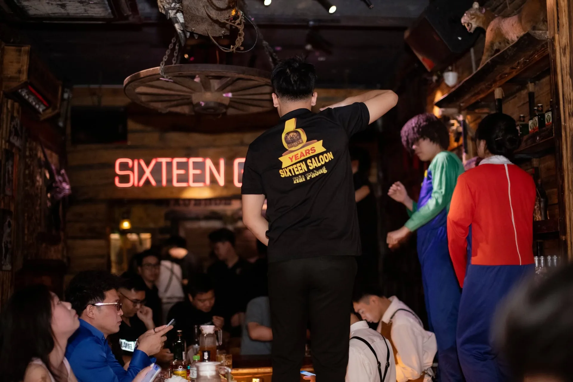 Biển chữ đỏ trên vách gỗ, bánh xe ngựa treo trần và đội ngũ áo kỷ niệm tại Sixsense